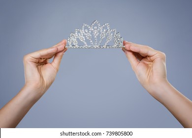 Shining diadem in female hands isolated on gray background