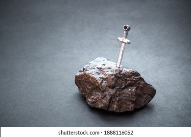 Shining Excalibur Sword In Stone Against Grey Grunge Background With Blank Space For Text. Copy Space. Legend Of King Arthur. Race, Struggle For Power