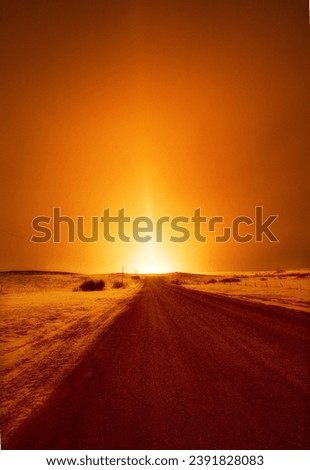 A shining fire light at the end of a road in the North Dakota winter. The snow creates a beautiful pillar of light from the burning natural gas flaring up from the ground. An ice trucking road. 