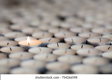 Shining light from a solitary burning candle flame. Selective focus on one flaming tealight among many extinguished candles.  