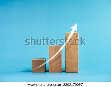 Shining rise up arrow on wooden cube blocks, bar graph chart steps on blue background, profit, benefit, income, business growth process, technology trend, economic improvement concepts, minimal style.