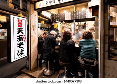 Shinjuku, Japan - April 4, 2019: Memory lane alley with izakaya pub and people sitting, drinking and eating by sidewalk in Tokyo city at night