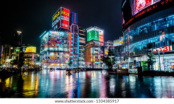 Shinjuku, Japan -\
November 20 2016: Traffic Junction near Shinjuku on a Rainy night\
with illumated lights from the surrounding buildings reflected off\
the water on the road