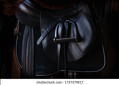 Shiny black leather horse saddle in the dark stable , with stirrup, ready for riding  - Powered by Shutterstock