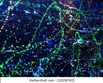 Shiny bright fluorescence art colorful drop and splash color water black light of dark black wallpaper of the glow in the dark disco night party. This seem the stars in the galaxy or cell and neuron.