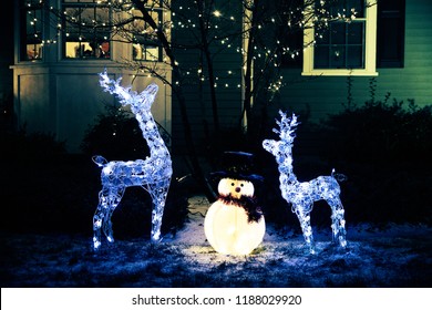 Shiny Christmas Decorations Outside At Night. Reindeer Family And Snowman. Christmas Background