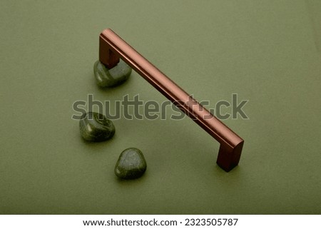A shiny copper pull handles and green natural stones on green surface