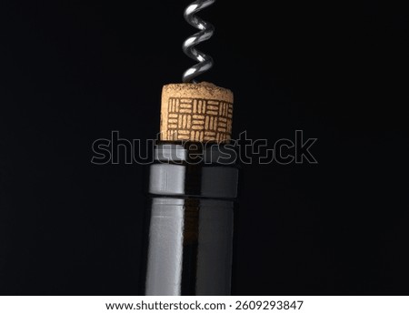 A shiny corkscrew pulls from a wine bottle, revealing rich amber tones as the cork lifts slowly. The dark background adds warmth to this intimate moment of celebration and connection.