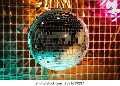 Shiny disco ball against foil party curtain under turquoise and orange light - Shutterstock ID 2331619237