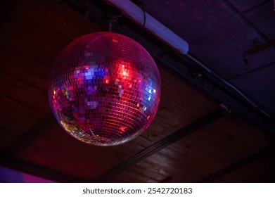 A shiny disco ball hanging from the ceiling, reflecting colorful lights across the room. The mirror tiles create vibrant patterns, adding a retro vibe perfect for parties, events, and dance floor. - Powered by Shutterstock