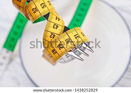 A shiny fork with a multicolored centimeter lifts from a white plate with a blue border. Paleodiet Concept