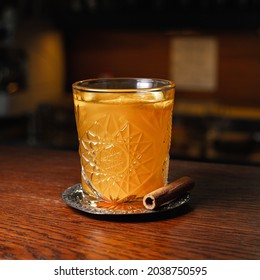 Shiny Glass Of Hot Orange Grog Cocktail With Cinnamon Stick Served On Wooden Counter In Cafe 