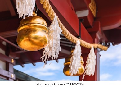 Shiny golden big suzu bells hung on a shimenawa rice or wheat straw rope adorned with suspended streamers known as shide and made with Japanese washi paper symbol of purity in a Shinto shrine. - Shutterstock ID 2111052353