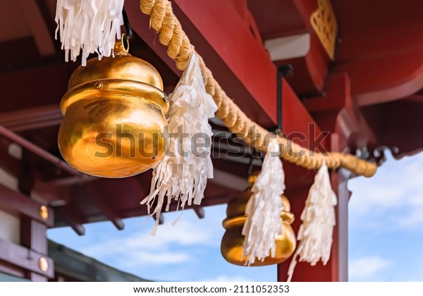 Shiny golden big suzu bells hung on a shimenawa
rice or wheat straw rope adorned with suspended streamers known as
shide and made with Japanese washi paper symbol of purity in a
Shinto shrine.