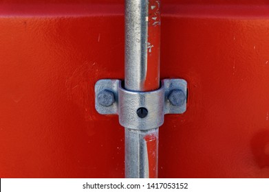 A Shiny Metal Bar Goes Through A C-clamp On A Bright Red Container