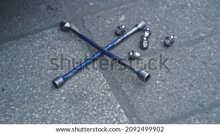Shiny Metal Security Lug Nuts for Car Wheel Hub Mounting Screws and Cross Wrench Laying on Ground Outside of Mechanic Workshop