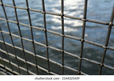 Shiny metal wire fence in front of blue water at dusk, close up