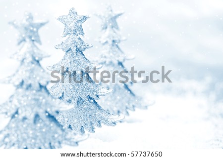 Shiny miniature tree ornaments on silver background with snow. High key blue toned macro with extremely shallow dof.  Copy space included.
