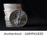 A shiny new American silver eagle coin in front of a stack of similar silver eagle coins