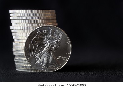 A Shiny New American Silver Eagle Coin In Front Of A Stack Of Similar Silver Eagle Coins