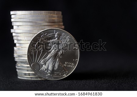 A shiny new American silver eagle coin in front of a stack of similar silver eagle coins