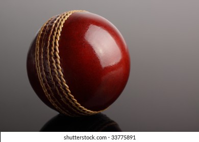 A shiny new cricket ball on a dark graduated background.