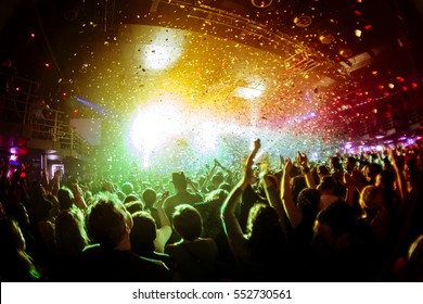 shiny rainbow confetti during the concert and the crowd of people silhouettes with their hands up