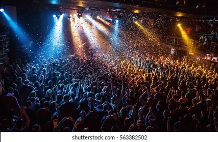 Shiny Rainbow Confetti During The Concert And The Crowd Of People Silhouettes With Their Hands Up. Dark Background, Smoke, Concert  Spotlights. Bright Lights