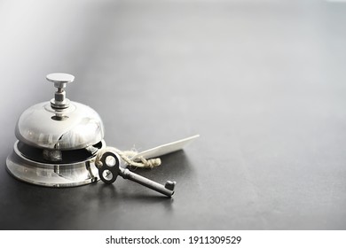 A Shiny Silver Metal Bell At Hotel Reception. A Table In The Hotel At The Concierge With A Bell And A Door Key. Key And Bell In A Hotel.