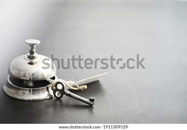 A shiny silver metal bell at hotel reception. A\
table in the hotel at the concierge with a bell and a door key. Key\
and bell in a hotel.