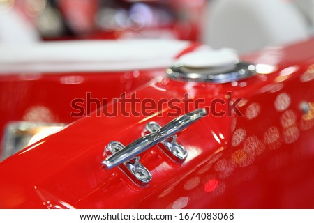 Shiny stainless mooring cleat on red plastic motor boat deck close up, marine equipment