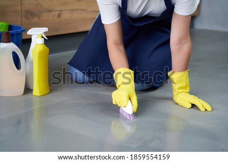 Shiny surface. Close up of hands of young woman in yellow gloves cleaning floor with detergents at home