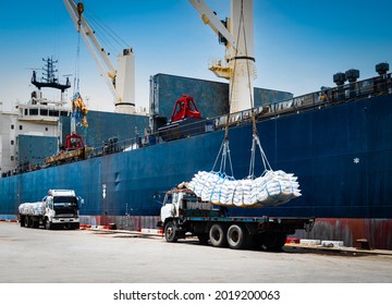 Ship crane lift-off slings of sugar bags cargo from truck and load into ship hold at seaport terminal for export. - Shutterstock ID 2019200063