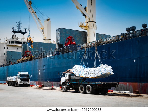 Ship crane\
lift-off slings of sugar bags cargo from truck and load into ship\
hold at seaport terminal for\
export.