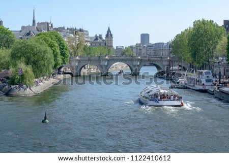 The ship is cruising on the Seine River in Paris. Behind it is Pont Neuf. Tourists admire the beauty of Paris from the boat and riverside of Seine. It is a beautiful sunny spring day in Paris, Europe
