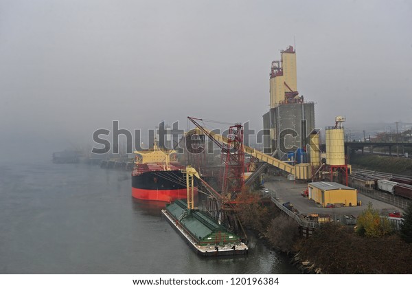 A ship is docked at a rail road yard with fog\
rolling in the background.