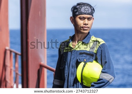 Ship engineer in protective uniform posing on deck of a merchant vessel during voyage at sea.
