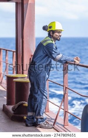 Ship engineer in protective uniform posing on deck of a merchant vessel during voyage at sea.