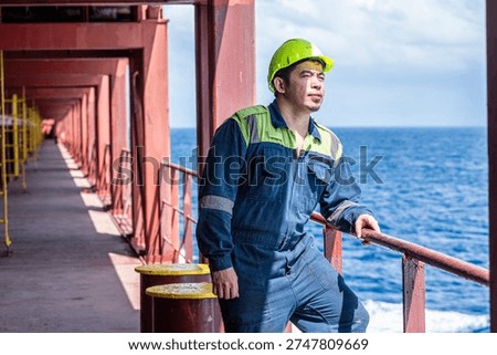 Ship engineer in protective uniform posing on deck of a merchant vessel during voyage at sea.