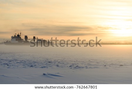 The ship is in the ice in the fog. A cargo ship is at sunset.