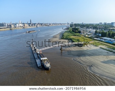 Ship moored at pontoon on the River Scheldt in Antwerp with barge and other boats in the background. City of Antwerp on one side, Linkeroever opposite