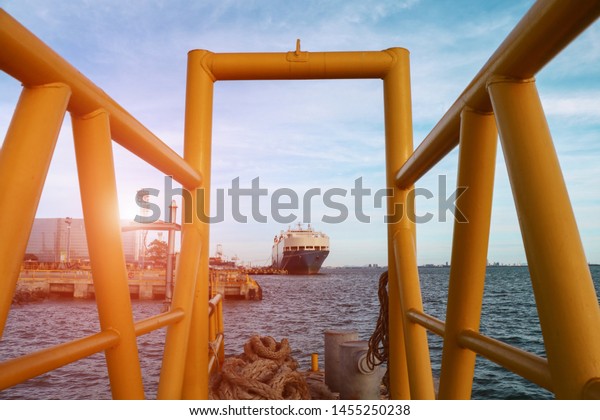 Ship moored in port, view through a skeletal steel\
frame of ship in the sea, Low angle front view of a large Auto car\
carrier ship moored alongside in port on blue sky with rope and\
anchor front ship.