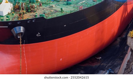 Ship on blocks in dry dock basin for maintenance and repairs. Hull freshly painted. Rusty anchor chain lowered to the bottom of dock. Close up view focus on bow. - Powered by Shutterstock