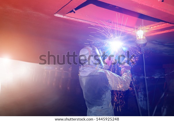 Ship Repair Industrial worker welding close up\
spark light for ship repair overhead position welding in shipyard\
under water ballast tank.