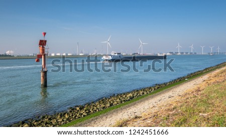 Ship sailing on the New Waterway along industries and wind turbines in the direction of the North Sea. This is the access route for large seagoing vessels from the North Sea to the port of Rotterdam.