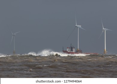 Ship Sailing In Rough Sea. High Cost Energy Of Offshore Wind Farm Turbines. Supply Vessel Battling Ocean Swell. Dangerous Waves For Shipping In Storm Conditions. Grey Sky Background With Copy Space