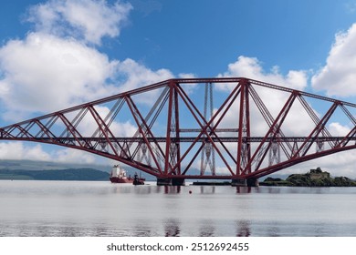 Ship sailing under the red Forth cantilever railway bridge across the Firth of Forth, Queensferry, UK near Edinburgh