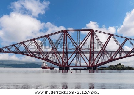 Ship sailing under the red Forth cantilever railway bridge across the Firth of Forth, Queensferry, UK near Edinburgh