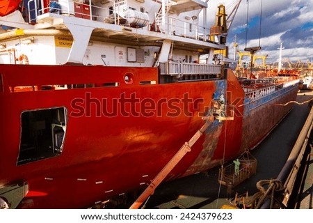 Ship undergoing maintenance in floating dock. Workers paint, repair vessel hull. Industrial, commercial shipyard activity during daytime. Maritime, nautical, shipbuilding business backdrop.