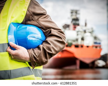 Shipbuilding Engineer Stands At The Dockside In A Port. Man Is Holding A Safety Helmet, Close-up.. Shipbuilding Industry